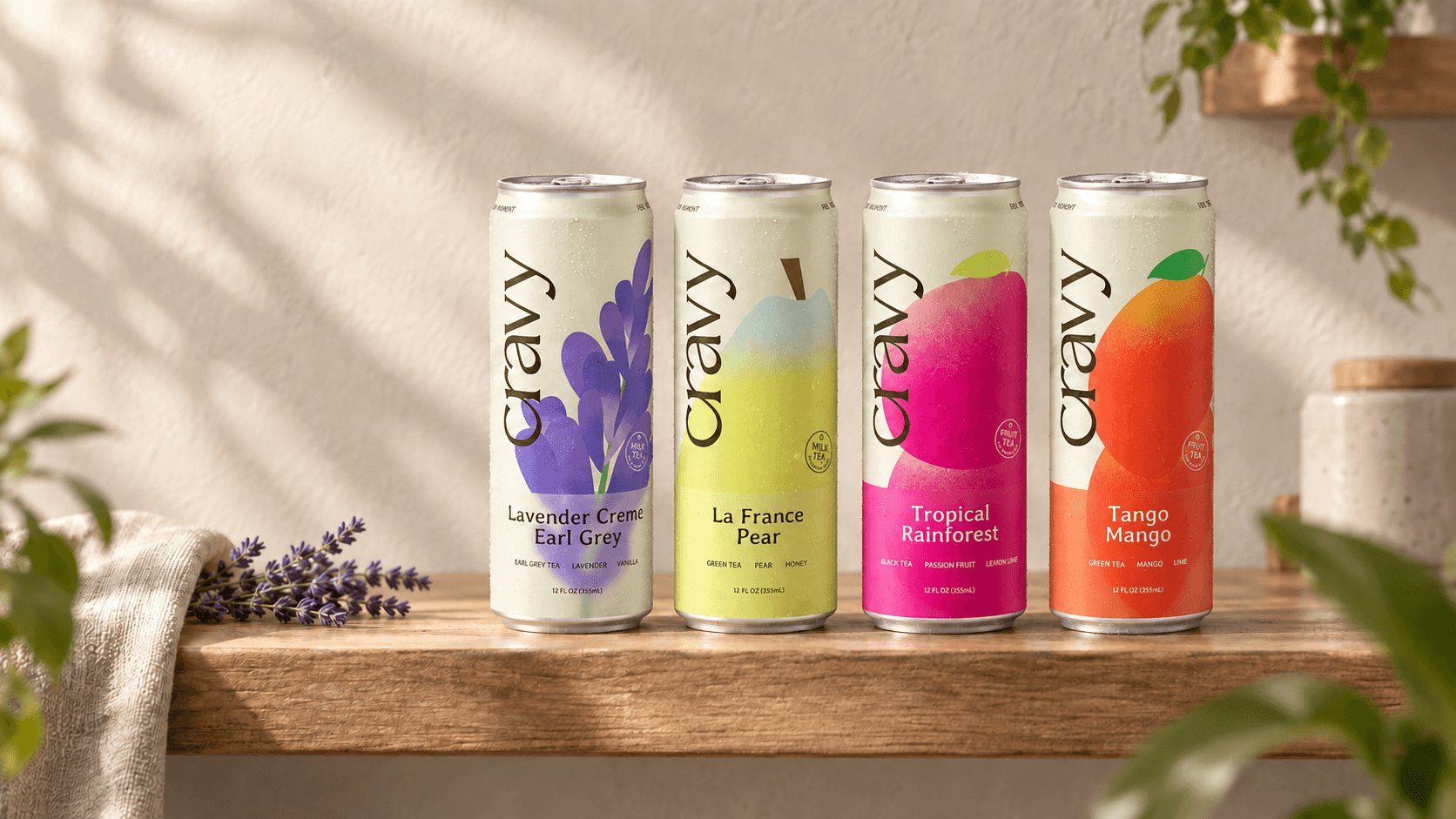 Four Cravy canned teas on a sunlit wooden shelf, surrounded by fresh lavender and greenery